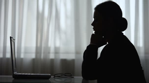 Silueta de mujer doblando las manos y mirando a la pantalla de la computadora portátil, pensando — Vídeo de stock