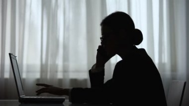 Dizüstü bilgisayarda not alma gece telefonda konuşurken iş kadını karanlık siluet