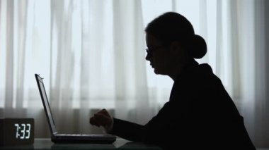Gece vardiyasını bitiren yorgun kadının silueti, dizüstü bilgisayar alarak odadan çıkıyor