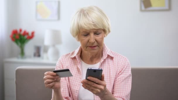 Positiv betagte Frau gibt Kreditkartennummer auf Smartphone ein, kauft online ein — Stockvideo