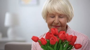 Sevimli yaşlı kadın lale demet koklama ve kamera gülümseyerek, mevcut