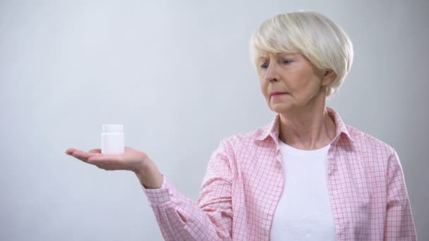 Upset senior woman holding pills bottle, unreliable pharmacological production — Stock Video