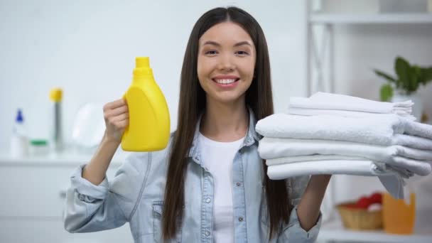 Χαμογελαστή γυναίκα που δείχνει καθαρές πετσέτες και απορρυπαντικό ρούχων, μαλακτικό υφασμάτων — Αρχείο Βίντεο
