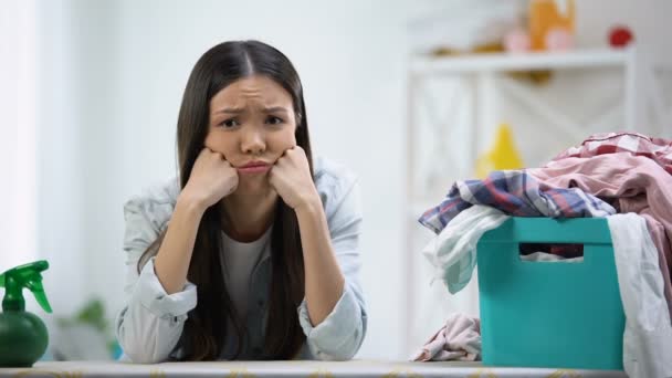 Boos huisvrouw kijken naar camera, wasmand vol kleren op tafel — Stockvideo