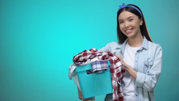 Cheerful woman holding laundry basket and smiling at camera, template for text — Stock Video