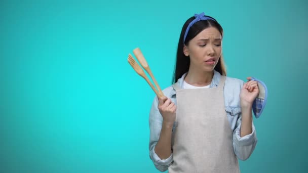 Incompetent housewife in apron holding kitchenware and shrugging shoulders — Stock Video