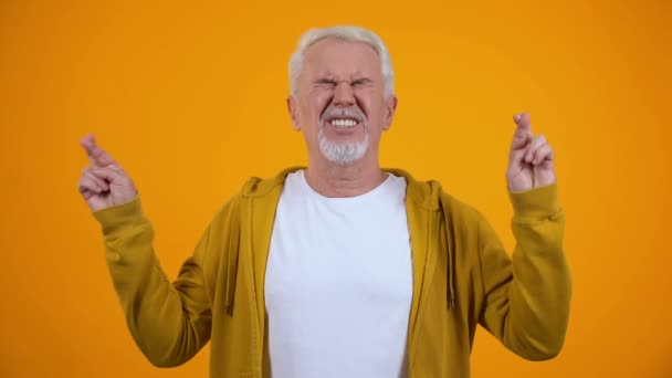 Male i hans 50s korsar fingrar för lycka, hoppas på seger, orange bakgrund — Stockvideo