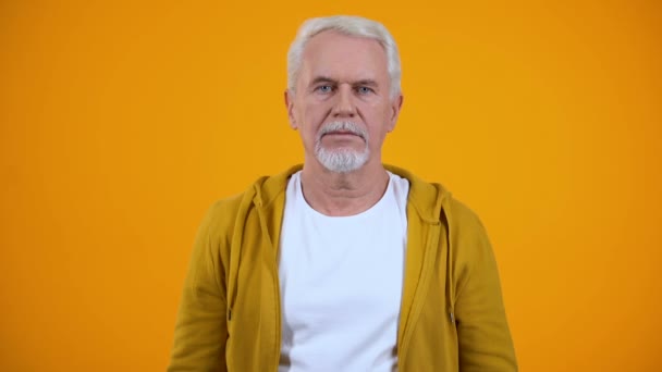Pensionista de pelo gris mostrando gesto de silencio sobre fondo naranja, secreto — Vídeo de stock
