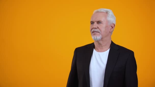 Feliz hombre viejo en traje disfrutando de un agradable aroma sobre fondo naranja, perfume — Vídeos de Stock