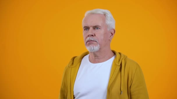 Седовласый пенсионер показывает пальмовый жест на оранжевом фоне, неудача — стоковое видео