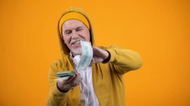 Šťastný starý muž v sluchátek a ve stylových šatech házel dolary a tancuje — Stock video