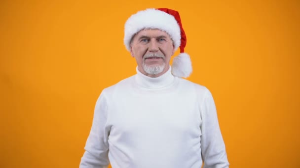 Щасливий сірий бородатий чоловік у капелюсі Санта Клауса, що показує жест мовчання та посміхається — стокове відео