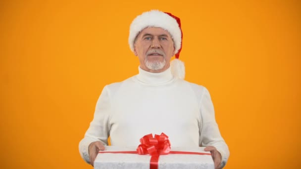 Noel Baba şapkalı nazik adam kamerada hediye kutusunu gösteriyor ve gülümseyen sürpriz — Stok video