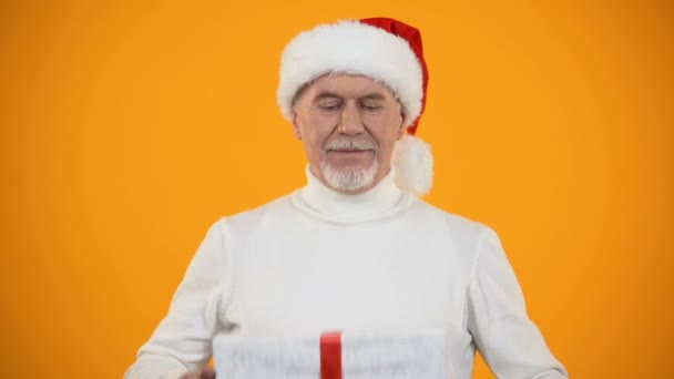 Hombre mayor complacido en santa hat abrazando giftbox, regocijando años nuevos sorpresa — Vídeo de stock