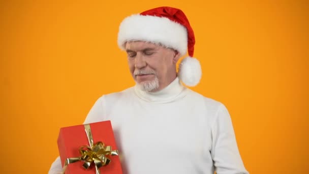 Sorridente pensionato maschio in cappello di Babbo Natale puntando il dito verso scatola regalo rossa, sconto — Video Stock