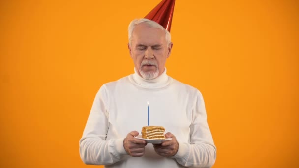 Solitario hombre mayor soplando vela en pastel de cumpleaños, tristemente mirando a la cámara — Vídeo de stock