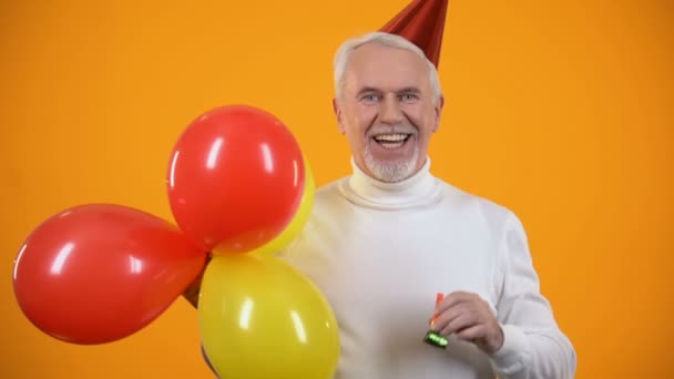 Fröhlicher Rentner mit Party-Gebläse und bunten Luftballons, Geburtstag — Stockvideo