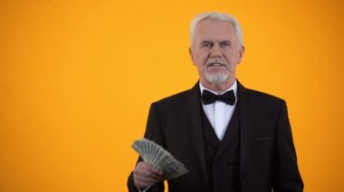 Takım elbiseli mutlu yaşlı adam dolar tutarak ve thumbs-up, iş geliri gösteren