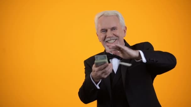 Glad elderly person in suit throwing dollar notes and smiling, good income, win — Stock Video
