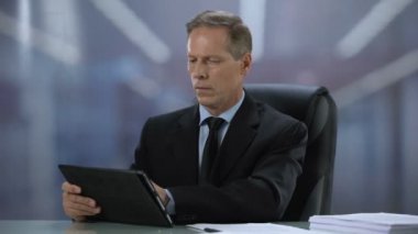 Ofis masasında tablet pc üzerinde çalışan kendinden emin erkek patron, online belgeler