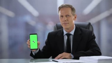 Kamera, iş uygulaması yeşil ekran akıllı telefon gösteren takım elbise neşeli erkek patron