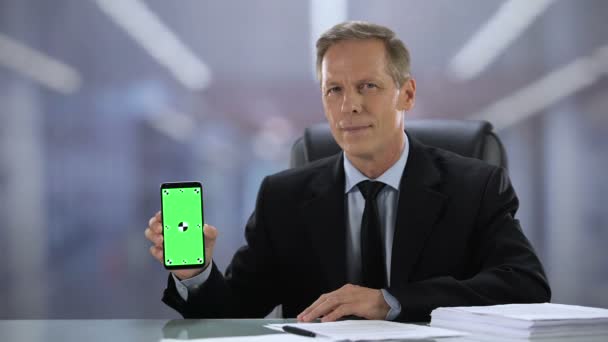 Alegre jefe masculino en traje que muestra el teléfono inteligente de pantalla verde en la cámara, aplicación de negocios — Vídeo de stock