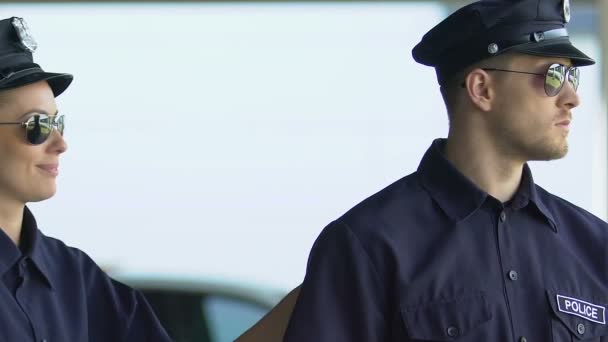 Männliche und weibliche Polizeibeamte mit Sonnenbrille lächeln in die Kamera, Stadtstreife — Stockvideo