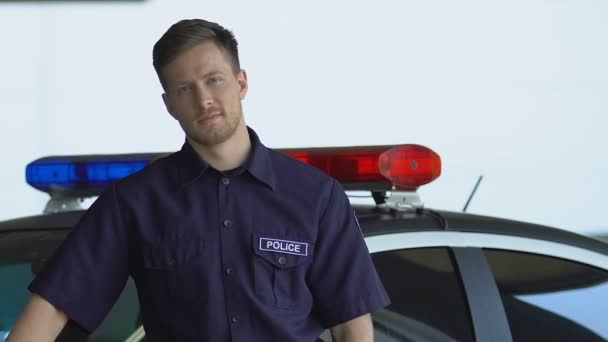 Snäll leende polis stående nära bilen och tittar in i kameran, kärleksfull jobb — Stockvideo