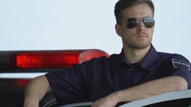 Poliziotto bello in occhiali da sole sorridente in piedi vicino all'auto, servizio di polizia affidabile — Video Stock