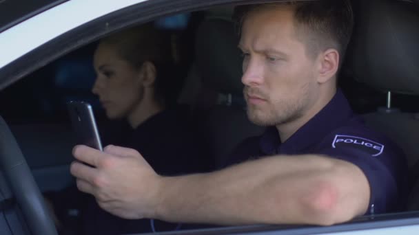 Полицейский следит за срочными вызовами по телефону, сидя с партнером в машине — стоковое видео