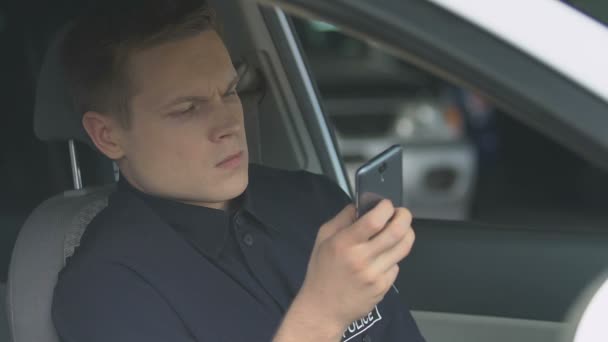 Поліцейський переглядає веб-сайти з новинами на смартфоні, сидячи в машині — стокове відео