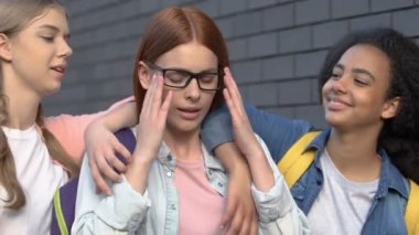 Kız öğrenciler akıllı kız öğrencinin omuzlarını iterek, gözlükle inekle alay ediyor
