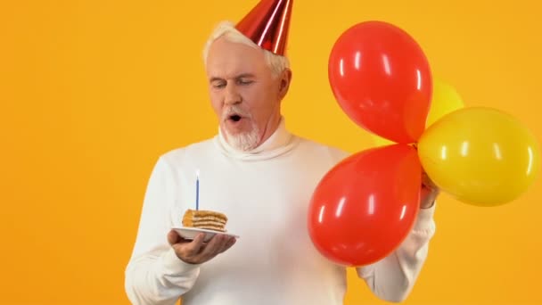 Smiling pensioner blowing cake candle falling confetti, birthday celebration — Stock Video