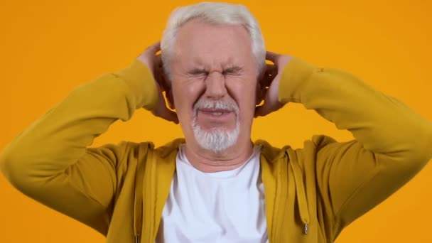 Старший чоловік покриває вуха руками, втомившись від гучного розмовного шуму, тиску — стокове відео