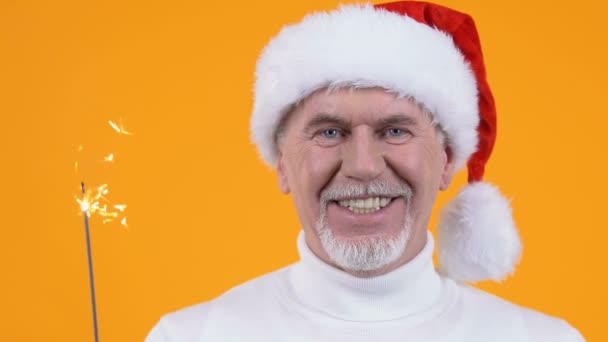 Sorridente uomo anziano cappello di Babbo Natale tenendo partito sparkler primo piano, celebrazione del nuovo anno — Video Stock