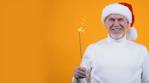 Hombre pensionista santa hat y bengala fondo naranja claro, saludo de Navidad — Vídeos de Stock