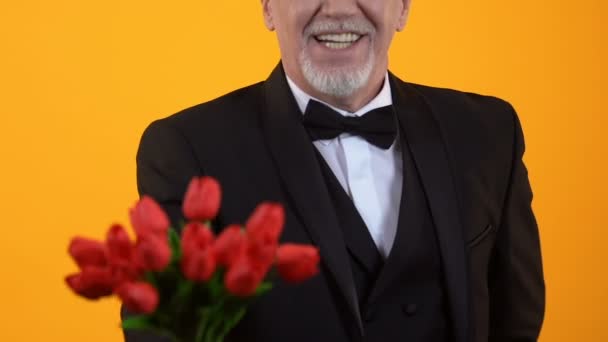 Glimlachend Senior man presenteert rode tulpen, welgemanierd gentleman op datum — Stockvideo