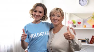 Yaşlı kadın ve kadın gönüllü başparmak gösteren ve sarılma, emekli yardım