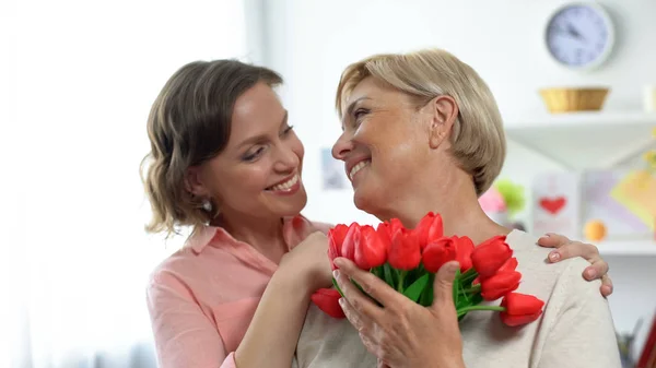 Uśmiechnięta Córka Przytulanie Starszy Matka Holding Tulipany Prezent Święto Pozdrowienia — Zdjęcie stockowe