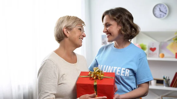 Senhora Sorridente Shirt Voluntária Dando Caixa Presente Para Senhora Idosa — Fotografia de Stock