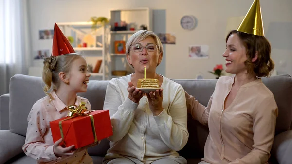 ケーキにキャンドルを吹くシニア女性 おばあちゃんを祝福する家族 お祝い — ストック写真