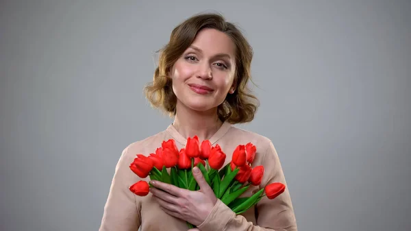 灰色の背景 休日の贈り物 女性らしさに微笑んで花を保持するかわいい女性 — ストック写真