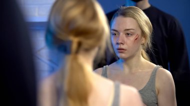 Yaralı yüzü arkasında duran erkek aynaya bakarak korkmuş kız