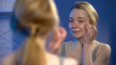 Depresif ağlayan kız ayna önünde yüz yarası kapsayacak şekilde kapatıcı uygulayarak