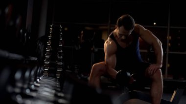 Güçlü iradeli vücut geliştirmeci yapıyor izole halter curl, akşam egzersiz oturmuş