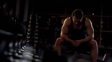 Vücut geliştirmeci egzersiz sonrası rahatlatıcı, spor kulübünde dumbbells yakınında oturan