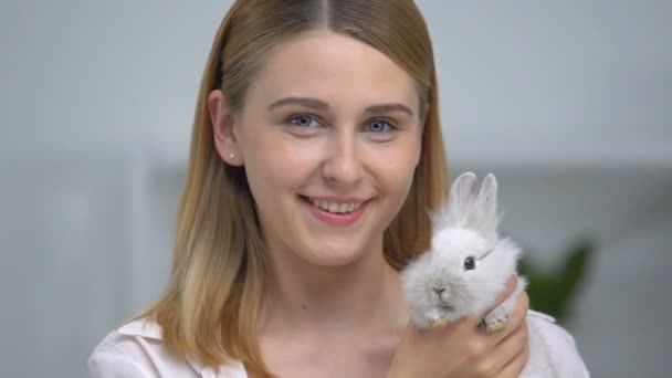 Happy girl holding fluffy rabbit and smiling on camera, pet adoption, friendship — Stock Video