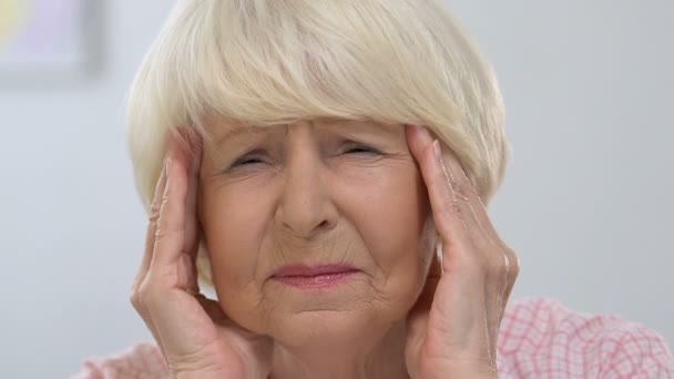 Elderly female massaging temples, suffering from migraine pain, health problem — Stock Video