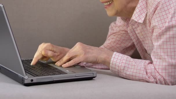 Улыбающаяся пожилая женщина наслаждается печатанием на ноутбуке, используя современные технологии, будущее — стоковое видео