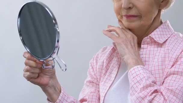 Alte Frau blickt in den Spiegel, berührt faltiges Gesicht, denkt über verlorene Schönheit nach — Stockvideo